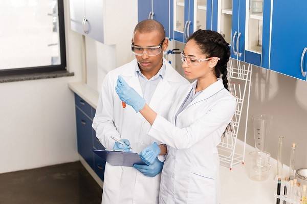 two black chemists, one male and one female, looking at a vial filled with red liquid