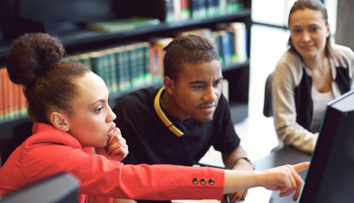 Three people in a library gathered around a computer monitor